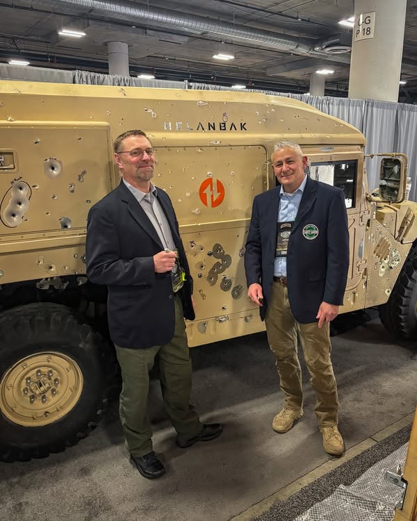 Two visitors standing beside the Helanbak Humvee at the SHOT Show booth