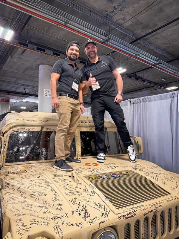 Two people standing on the hood of the Helanbak Humvee, covered in signatures